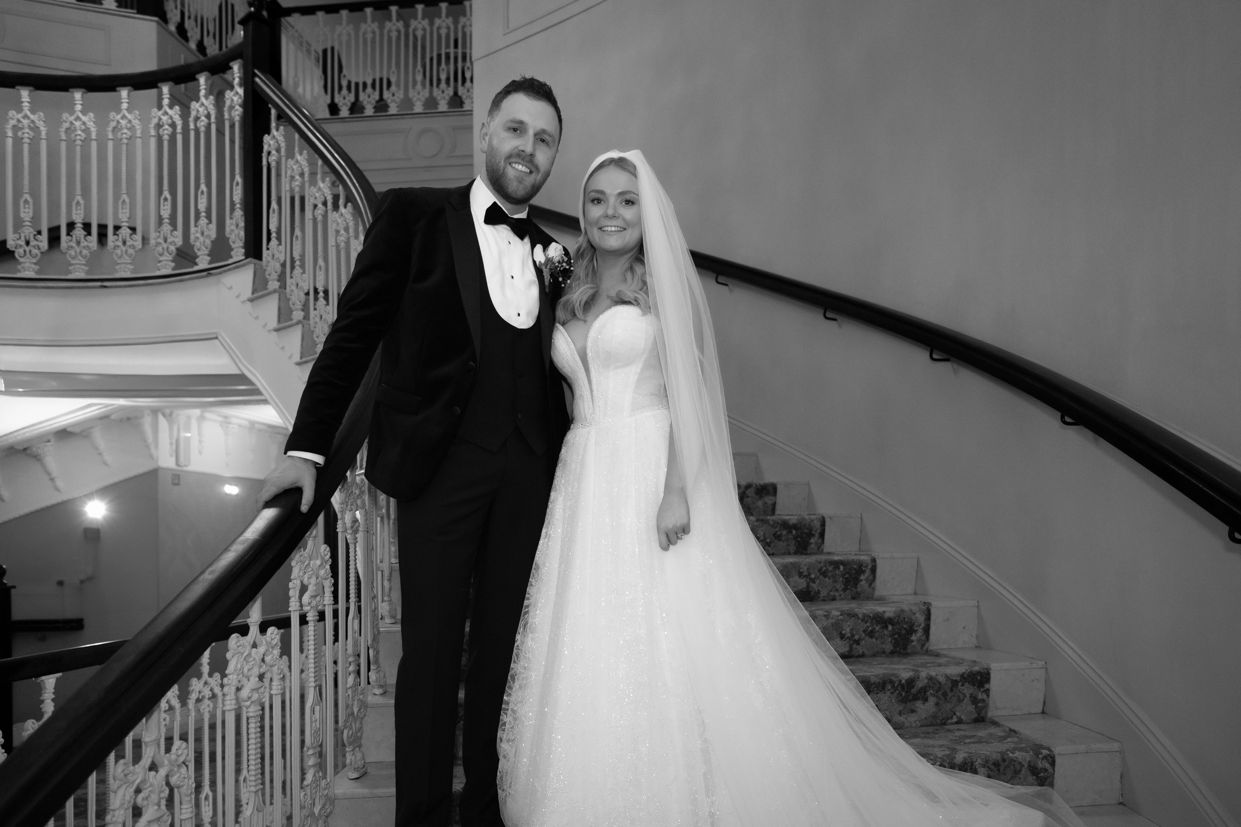 A bride and groom standing on a staircase at their wedding, smiling for the camera.
