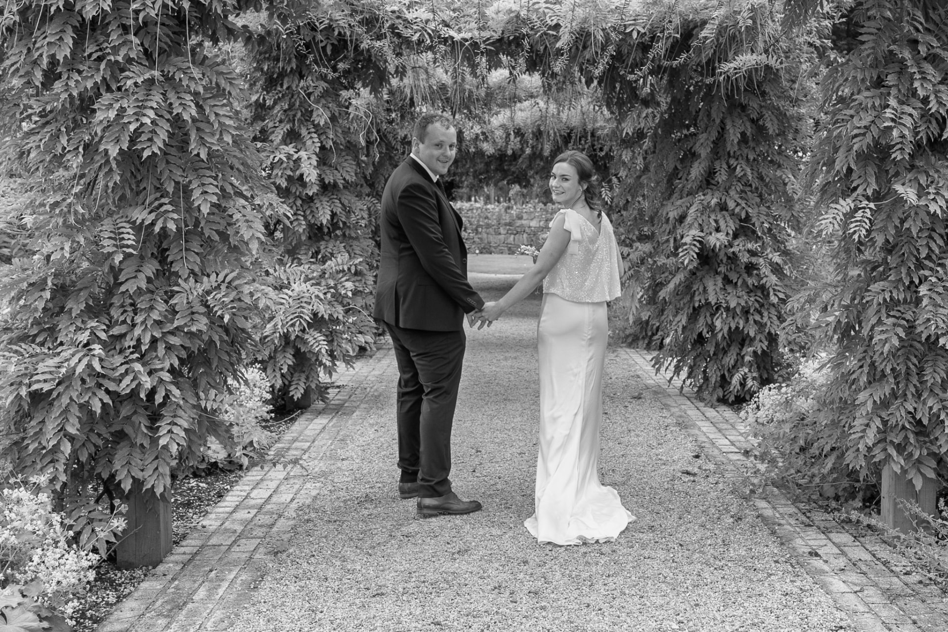 Black and white portrait of a couple beneath a wisteria walkway