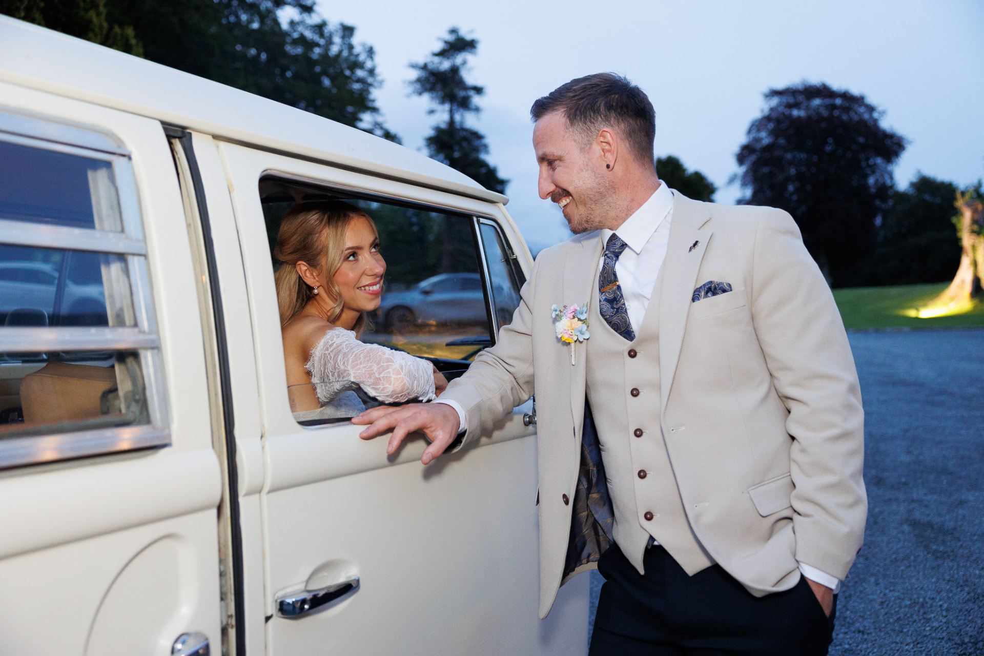 Groom leaning on a vintage camper van at dusk