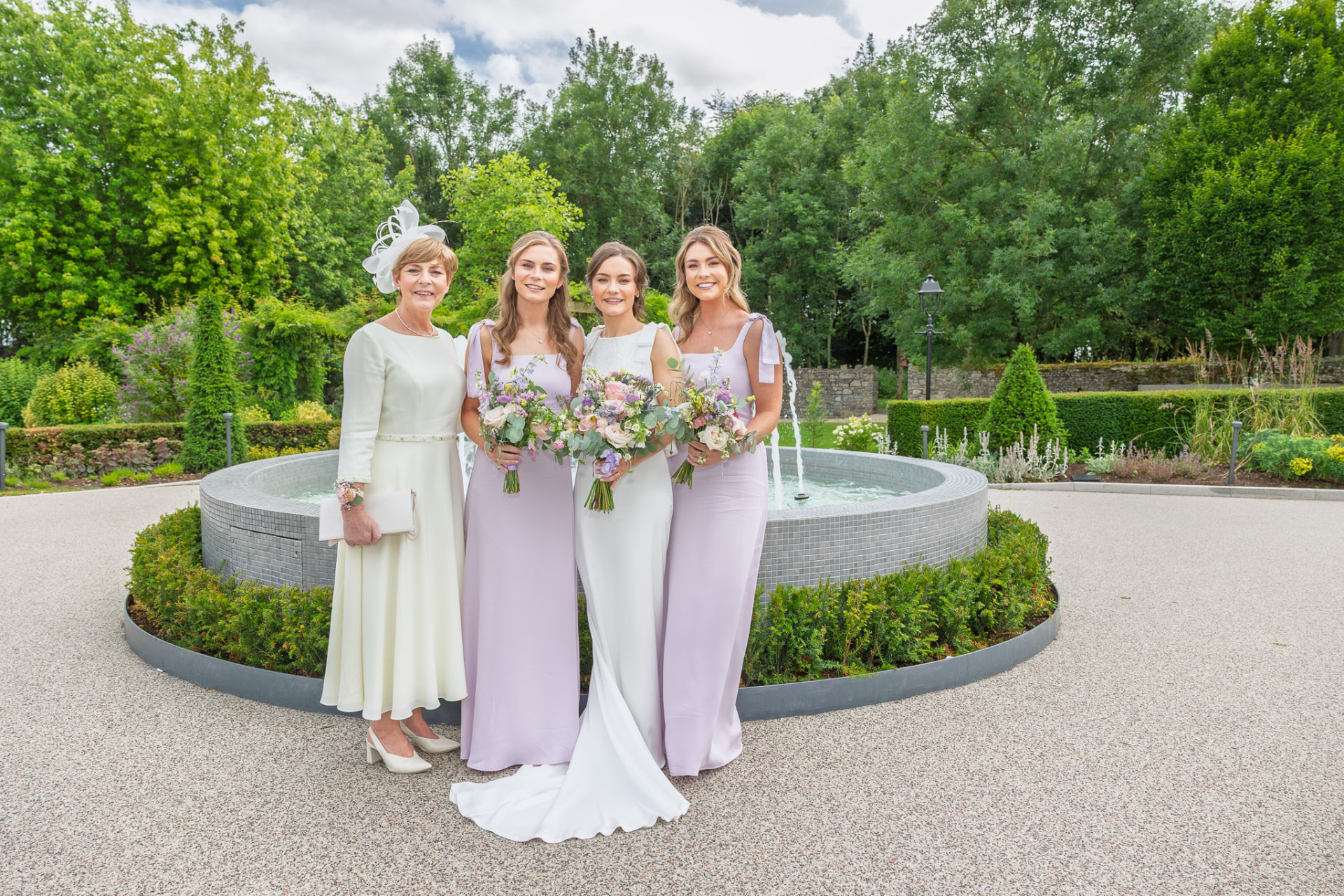 Bride with her bridesmaids and mother beside a garden fountain