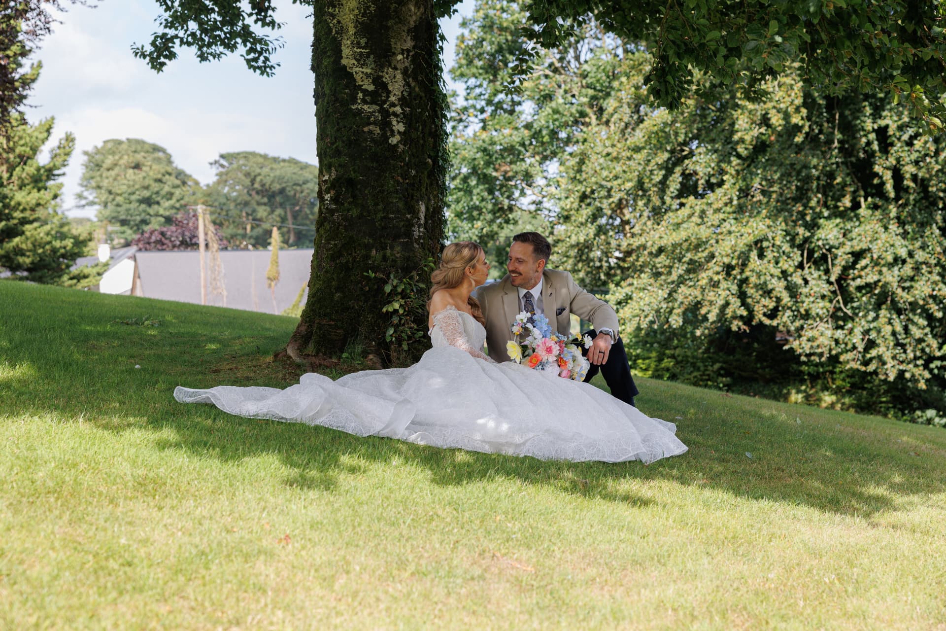 Couple sitting together on the grass beneath a large tree