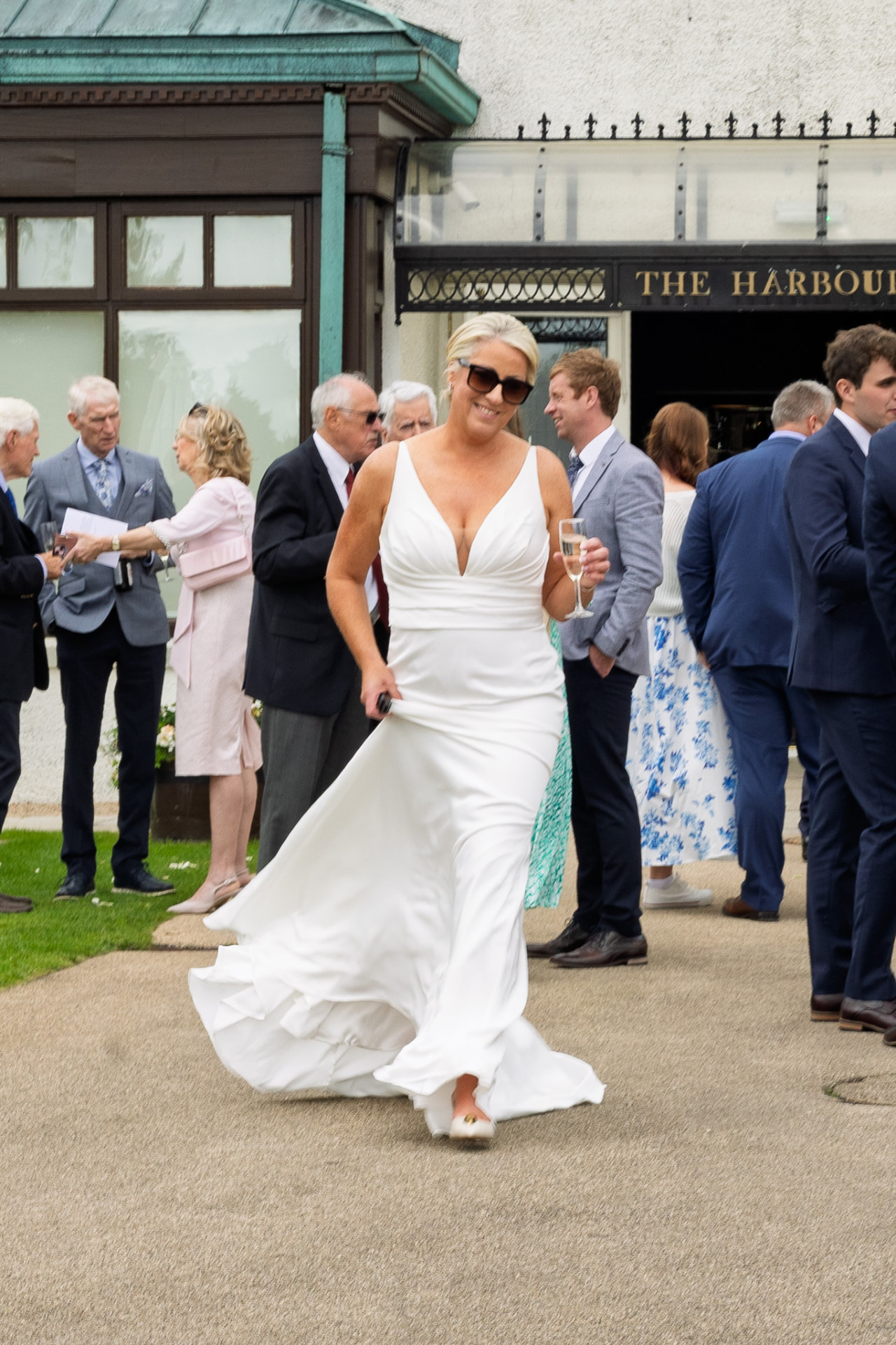 Bride crossing the courtyard with a glass of champagne during drinks reception
