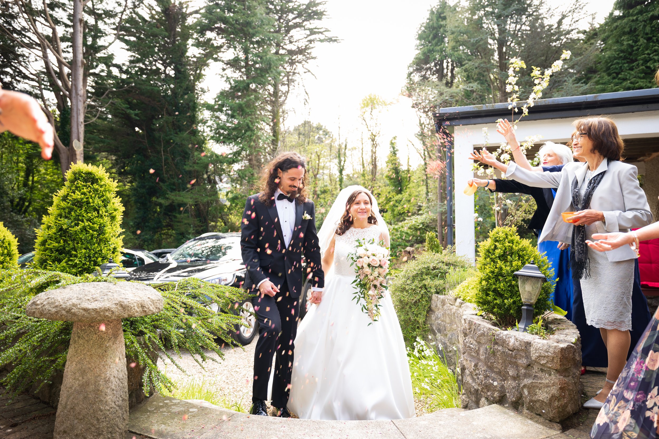 A bride and groom walking outside while guests throw flower petals in celebration of their wedding.