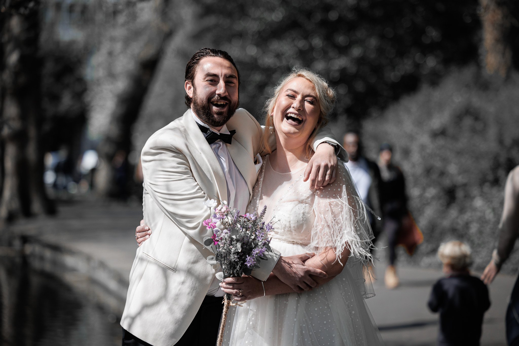 A happy couple on their wedding day, with the groom in a white tuxedo and the bride in a white wedding dress, smiling and embracing outdoors.