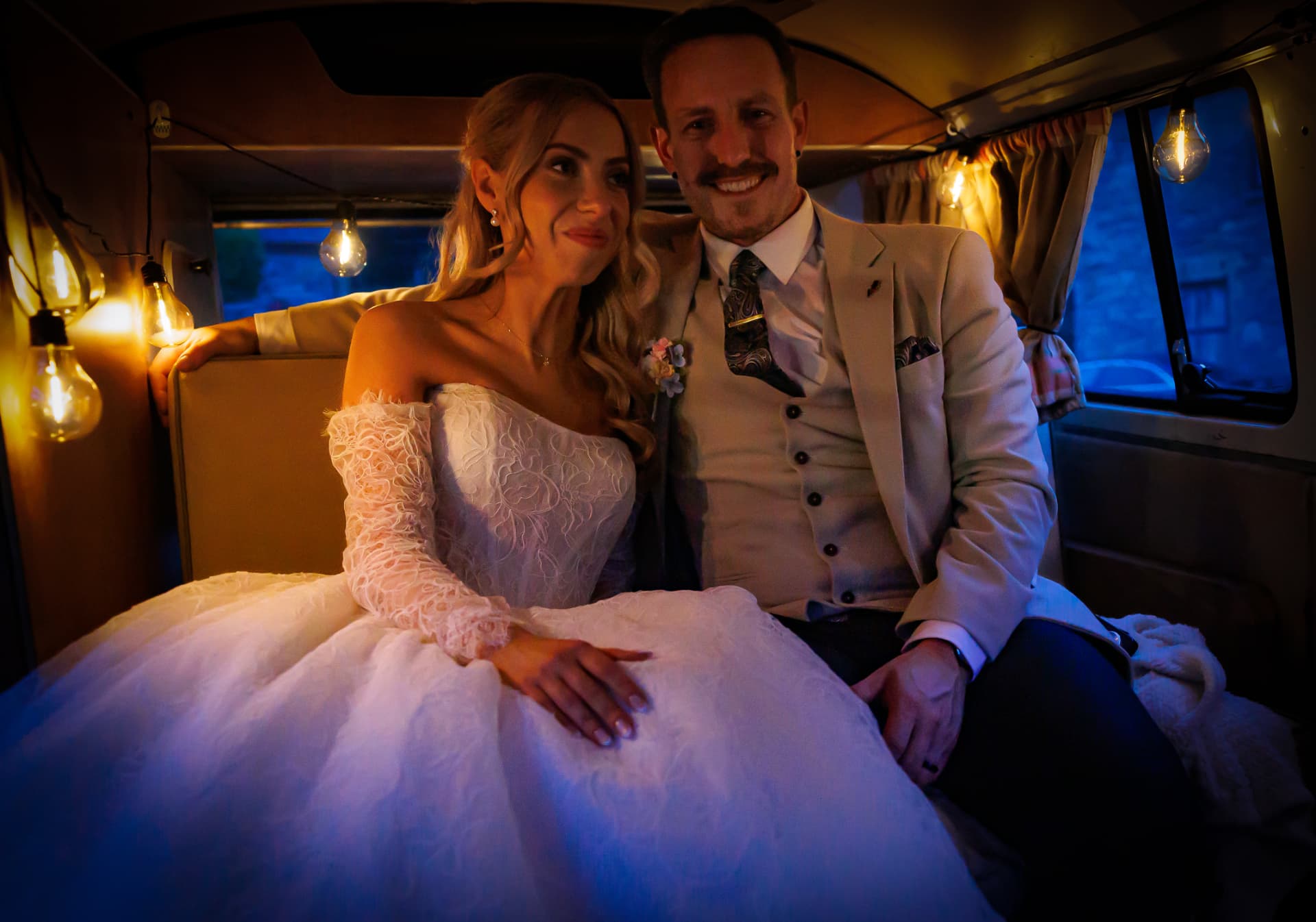 Couple sitting in a festoon-lit vintage camper van at dusk