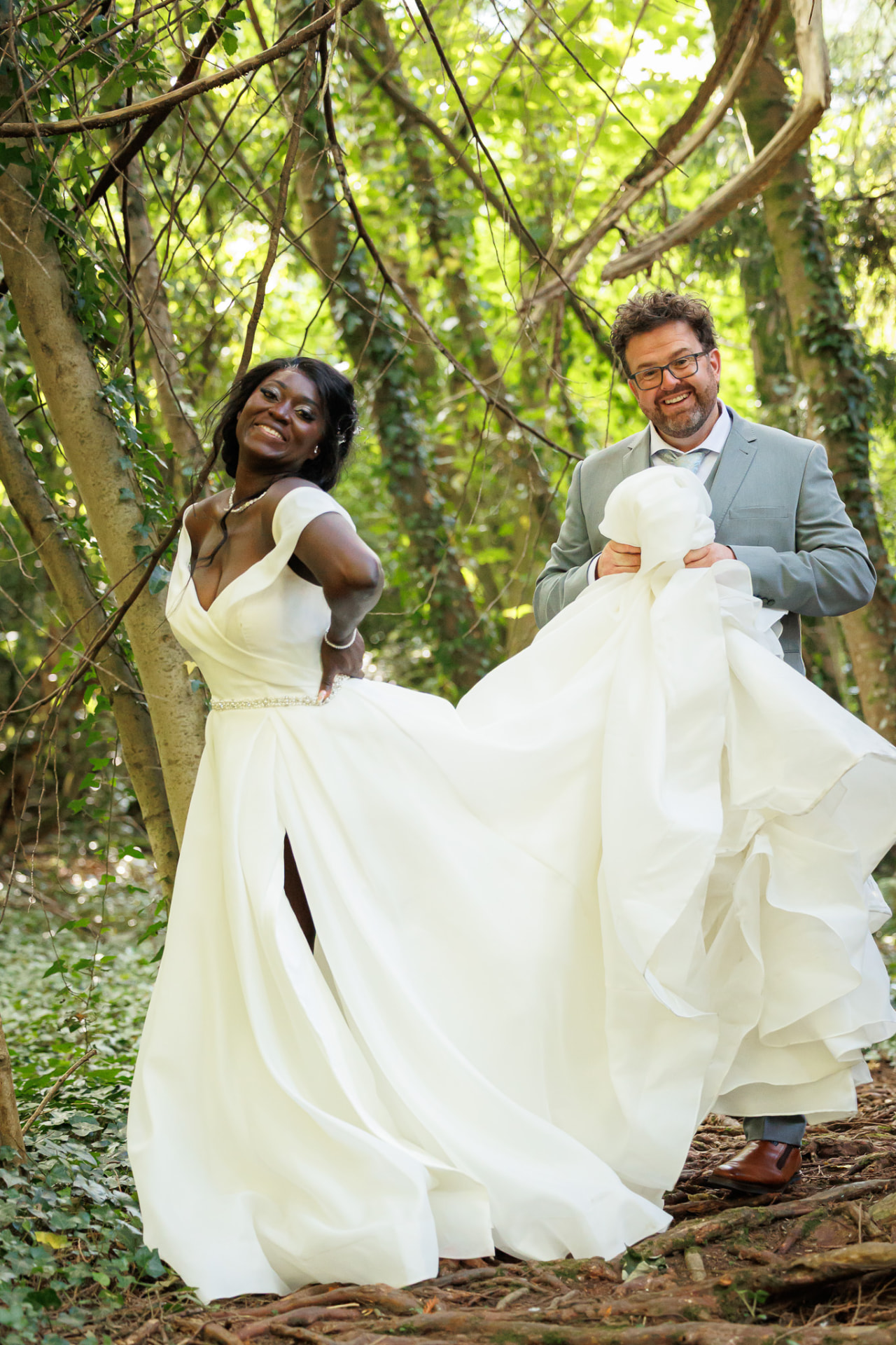 Groom lifting the bride's dress in woodland