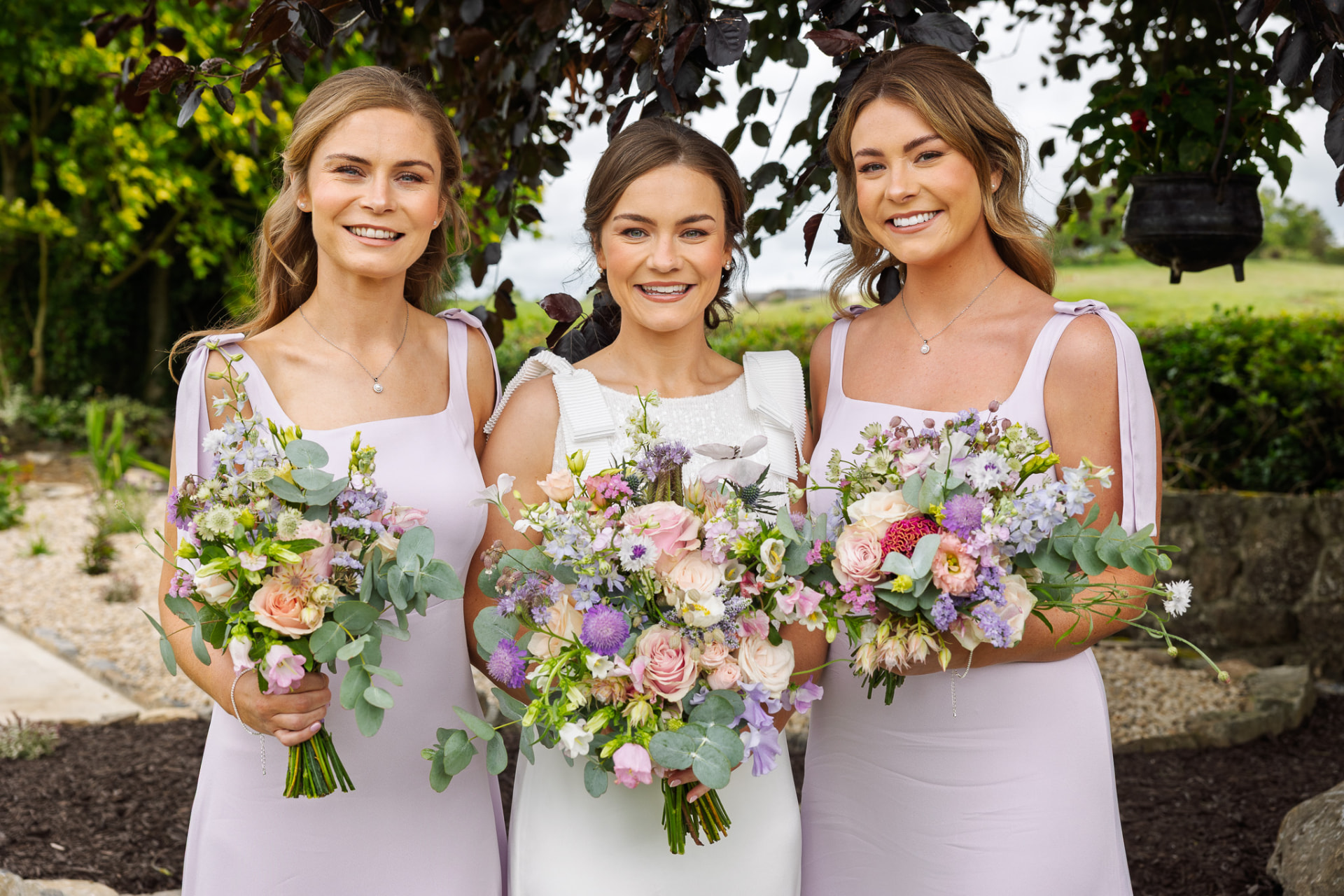 Bride with her two bridesmaids holding wildflower bouquets in a summer garden