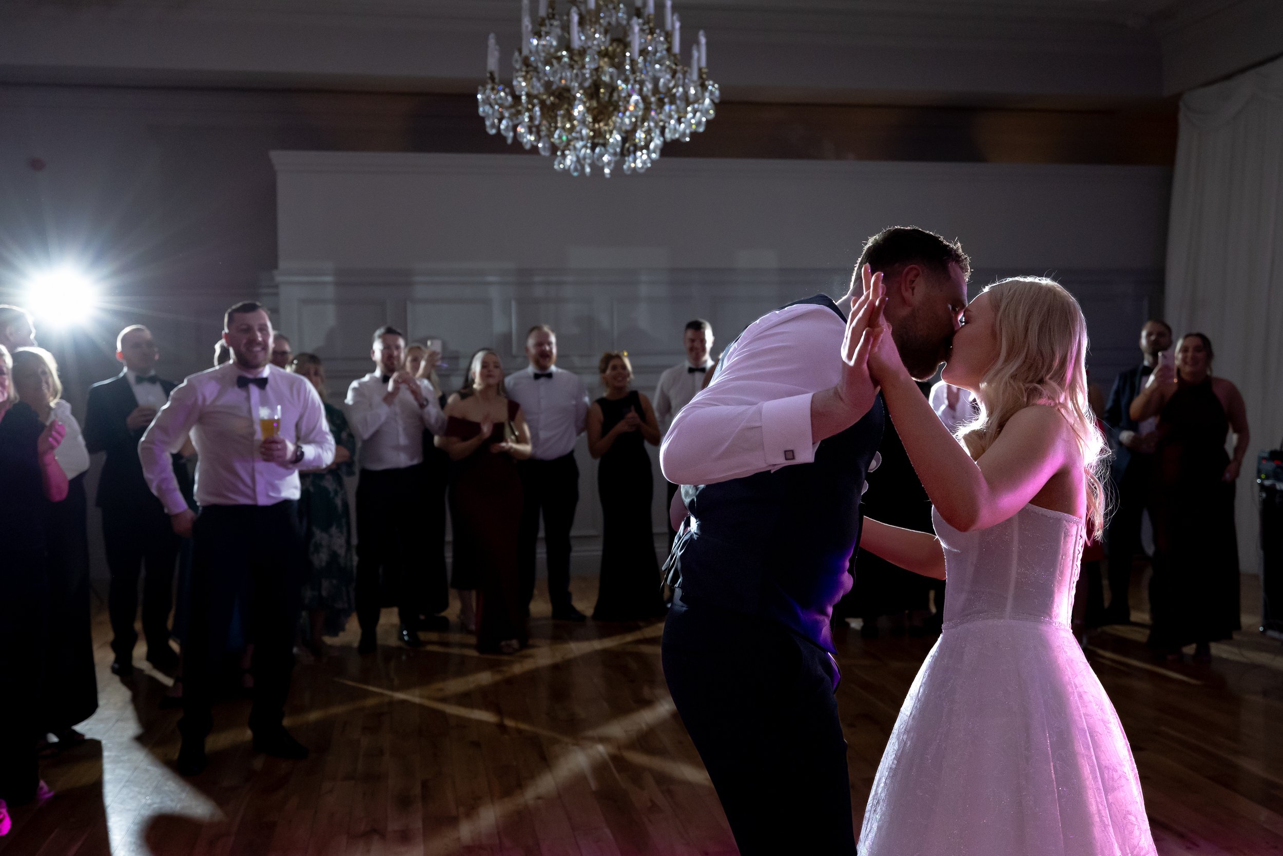 A bride and groom sharing their first dance at a wedding reception, surrounded by wedding guests in formal attire watching and enjoying the moment.