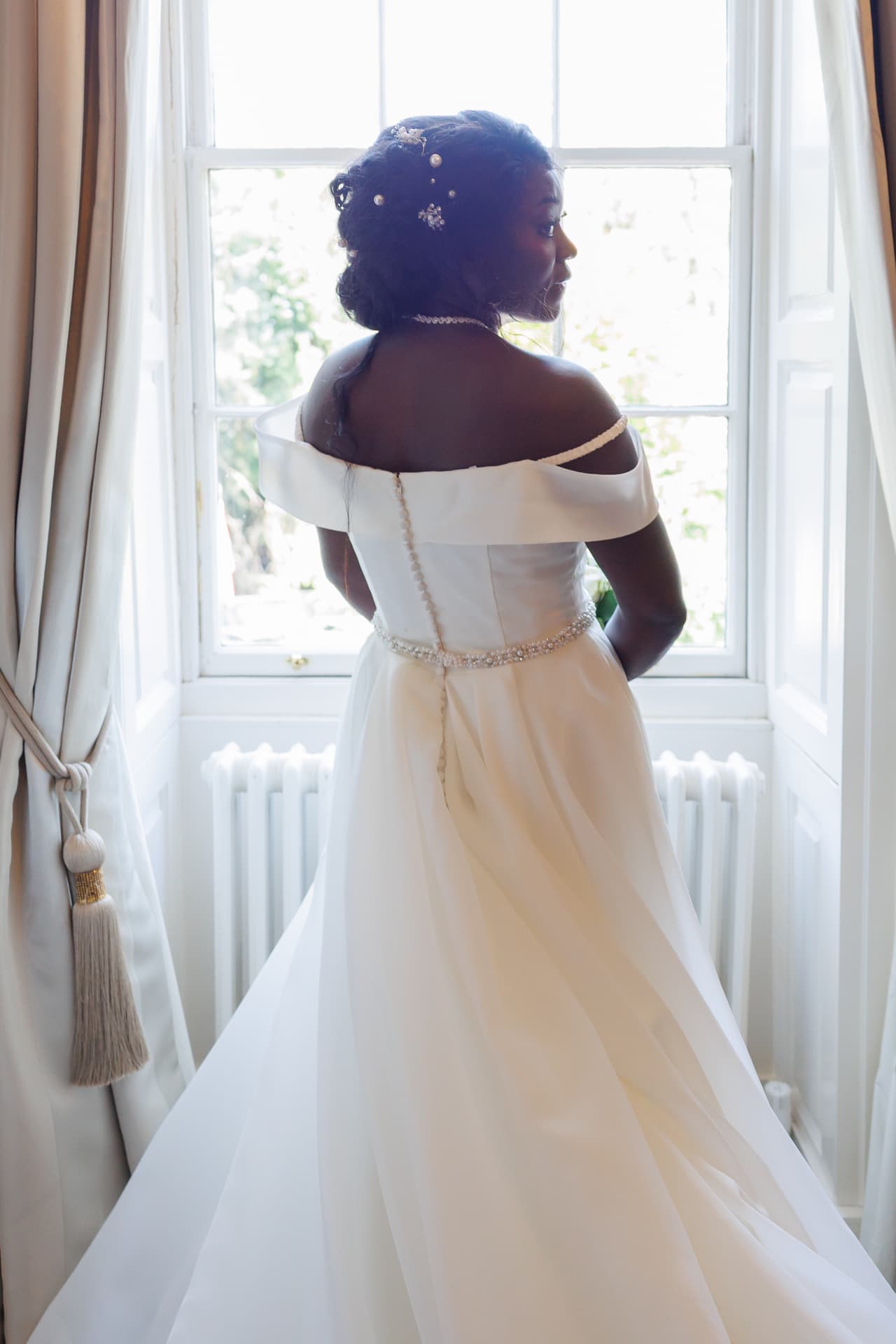 Bride in an off-shoulder gown looking out a Georgian sash window